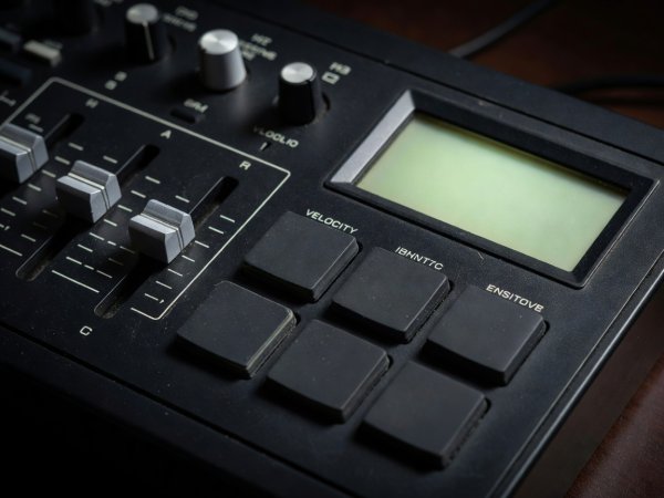 Close-up of vintage drum sampler tuning sliders and numbered velocity pads next to a backlit LCD screen