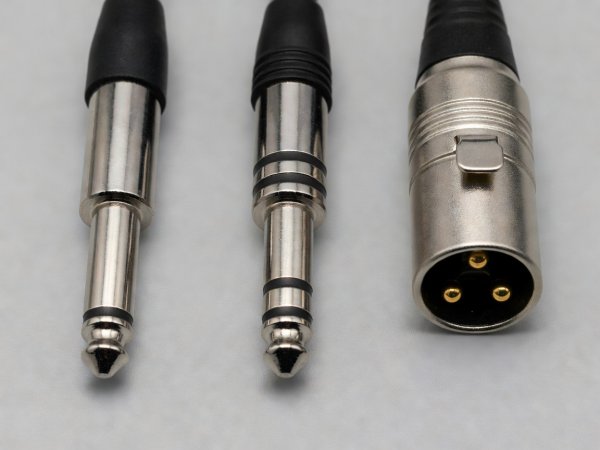 Side-by-side macro comparison of a 1/4-inch TS mono plug with one black insulating ring, a 1/4-inch TRS balanced plug with two rings, and a 3-pin male XLR connector